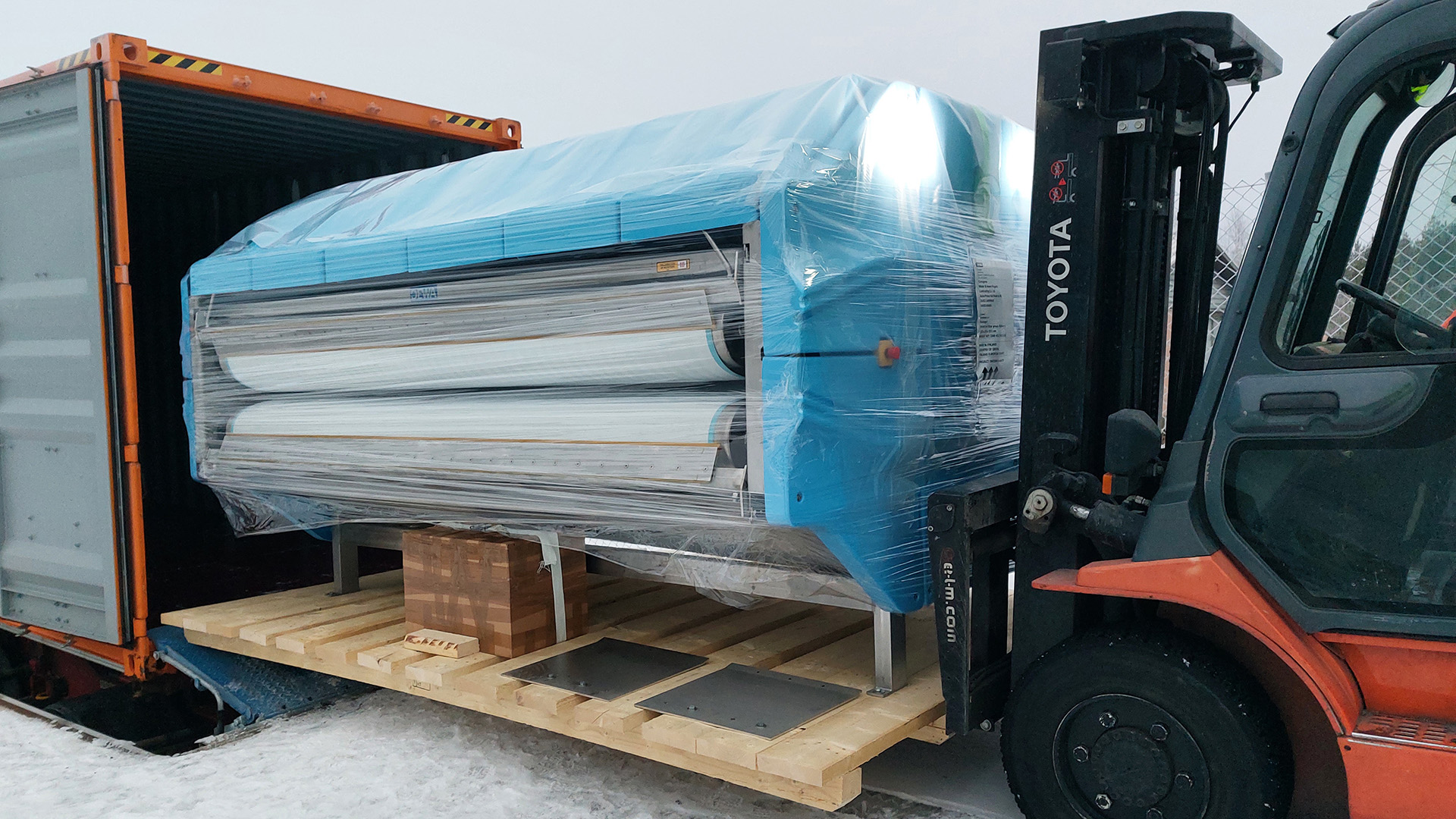 AURA PRESS 26 belt filter press being loaded into a standard shipping container at Dewaco's facility, demonstrating efficient sludge dewatering equipment with container-optimized design for global transport.